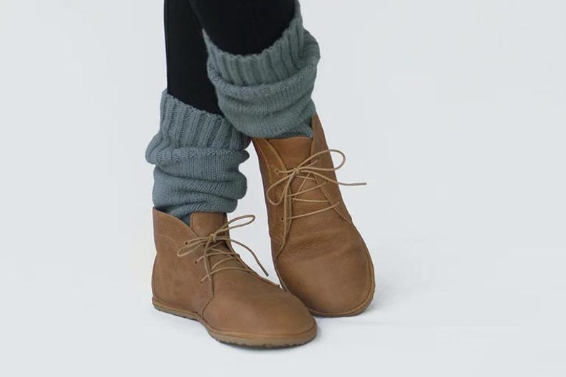 May include: A pair of brown leather ankle boots with laces. The boots are worn with gray knitted leg warmers.