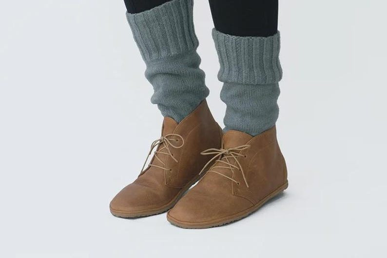 May include: A pair of brown leather ankle boots with laces. The boots are worn with gray knitted leg warmers.
