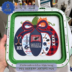 May include: An embroidery design of a pumpkin featuring hockey-themed elements including sticks, a net, skates, and the text "GOAL!", "ICE", and "HOCKEY". The design is secured in a green embroidery hoop with size options 4", 5", 6", 7", 8".