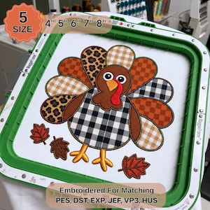 May include: A green MaggieFrame embroidery hoop containing a fabric panel with a turkey design. The turkey features a black and white buffalo plaid body and multi-patterned tail feathers in leopard print, gingham, and plaid. Includes three autumn leaves.