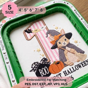 May include: An embroidery design in a green MaggieFrame hoop featuring a large number one with pink stripes, a rabbit wearing a witch hat and cape holding a broom, a pumpkin, a black ornament with the text BOO, and small bats and stars.
