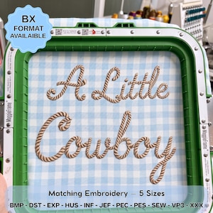 May include: A green embroidery hoop holding light blue and white gingham fabric with the embroidered text A Little Cowboy in a tan rope-style font. The frame includes metal hardware and a blue label stating BX FORMAT AVAILABLE.