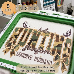 May include: An embroidery hoop containing fabric with the stitched text "HELLO HUNTING SEASON GOODBYE HUSBAND" in brown, featuring camouflage-patterned letters, two bows, and deer antlers. The hoop is green and includes 5 size options: 10.16 cm, 12.7 cm, 15.24 cm, 17.78 cm, 20.32 cm.
