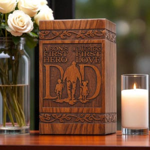 Puede incluir: Una urna de madera con la palabra "DAD" tallada en la parte delantera, junto con las palabras "A SON'S FIRST HERO" y "A DAUGHTER'S FIRST LOVE". La urna tiene un diseño floral decorativo y está junto a un jarrón de rosas blancas y una vela encendida.