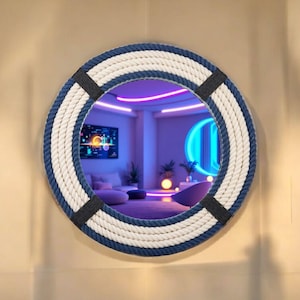 May include: Circular mirror with a nautical theme, featuring a rope design. The frame has alternating bands of white and navy blue rope, held together by black sections. The mirror reflects a room with neon lighting and contemporary furniture.