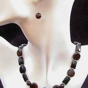 May include: A necklace and earrings set featuring brown and black gemstone beads. The necklace has a silver chain and the earrings are silver hook style.