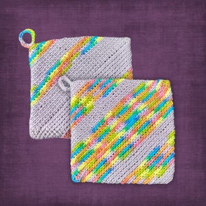 May include: Two gray, square crocheted potholders with colorful diagonal stripes in shades of yellow, orange, pink, blue, and green. Each potholder has a small loop for hanging. The background is a solid purple.