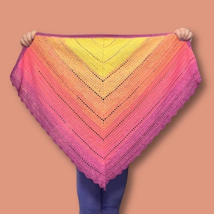May include: A triangular crochet shawl featuring a vibrant gradient color pattern that transitions from a bright yellow center to orange, pink, and deep purple at the edges. The shawl has a textured stitch pattern and a scalloped border edge.