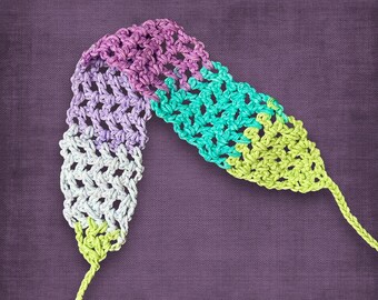 May include: A handmade crochet strap in a gradient of colors, including purple, teal, and green. The strap is made with a woven pattern and has a textured appearance. The strap is likely for a camera or bag.