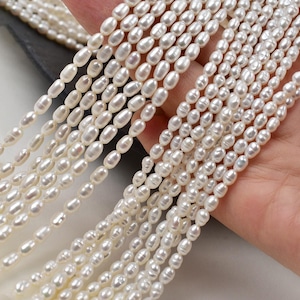 Può includere: Fili di perle ovali bianco crema lucenti. Le perle sono infilate, creando più file. Le perle hanno una superficie liscia e lucida e una leggera lucentezza. L'immagine mostra la bellezza naturale delle perle, ideali per la creazione di gioielli.