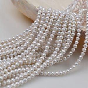 May include: Strands of lustrous, white pearls. The pearls are small and round, with a smooth surface. The strands are draped over a white surface, creating a cascading effect. The pearls are a classic and elegant accessory.