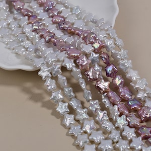 Op de afbeelding: Strengen stervormige parels in witte en roze tinten. De parels hebben een glanzende afwerking en zijn aan elkaar geregen, waardoor een delicate en elegante uitstraling ontstaat. De parels worden gepresenteerd op een wit oppervlak.