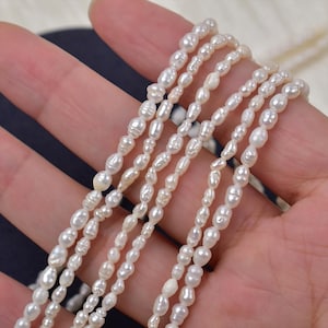 Pode incluir: Várias fileiras de pérolas brancas em forma oval. As pérolas são enfiadas, criando um design delicado de colar ou pulseira. As pérolas têm um brilho natural e tamanhos variados, sugerindo uma origem artesanal ou orgânica.