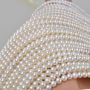 Pode incluir: Close-up de vários fios de pérolas brancas. As pérolas são redondas e têm um brilho lustroso. A imagem mostra uma grande quantidade de pérolas, sugerindo que são para fazer joias ou para venda.