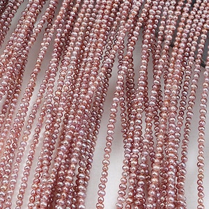 Op de afbeelding: Close-up van meerdere strengen roze zoetwaterparels. De parels zijn klein, onregelmatig van vorm en aan elkaar geregen. De kleur is een zacht, stoffig roze, en de strengen hangen verticaal, waardoor een getextureerd, gelaagd effect ontstaat.