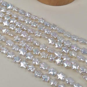 Op de afbeelding: Close-up van strengen witte, stervormige kralen met een parelmoerglans. De kralen zijn aan elkaar geregen, waardoor een textuur en glinsterend effect ontstaat. Ideaal voor het maken van sieraden, deze kralen bieden een uniek hemels ontwerp.