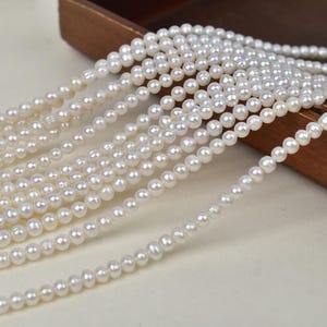 May include: Strands of small, white pearls cascade from a wooden container. The pearls are uniform in size and have a lustrous sheen. The image showcases the delicate beauty of the pearls, suggesting jewelry or craft supplies.