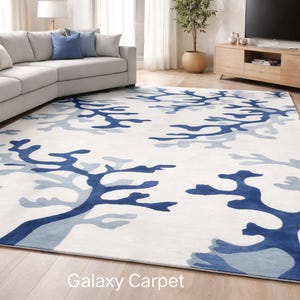 Op de afbeelding: Een groot, rechthoekig vloerkleed met een witte achtergrond en een patroon van blauwe koraalachtige vormen. Het vloerkleed ligt in een woonkamer met een bank, stoelen en een televisie. De tekst "Galaxy Carpet" is zichtbaar.