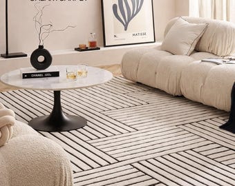 May include: A modern living room featuring a cream-colored sofa and a round marble coffee table. A black and white striped rug covers the floor. A framed art print hangs on the wall. The text "GALAXYCARPET" is visible.
