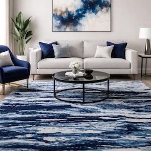May include: A modern living room featuring a light gray sofa with navy blue and white accent pillows. A round black coffee table sits on a blue and white patterned rug. An abstract painting hangs above the sofa.
