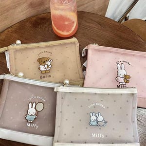 Op de afbeelding: Een verzameling make-up tasjes met ritssluiting met het Miffy-personage van Dick Bruna. De tasjes zijn in pastelkleuren zoals beige, roze en grijs, met geborduurde Miffy-ontwerpen en de naam "Miffy" of "Boris". Elke tas heeft een parelritssluiting.
