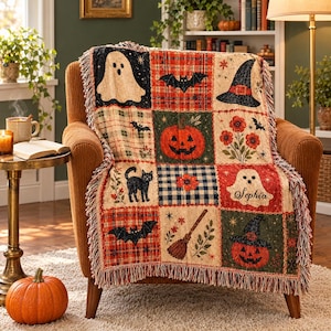 May include: A woven throw blanket featuring a grid of Halloween-themed squares including ghosts, bats, a witch hat, a jack-o'-lantern, a black cat, flowers, and a broomstick. One ghost square includes the name Sophia in cursive script.