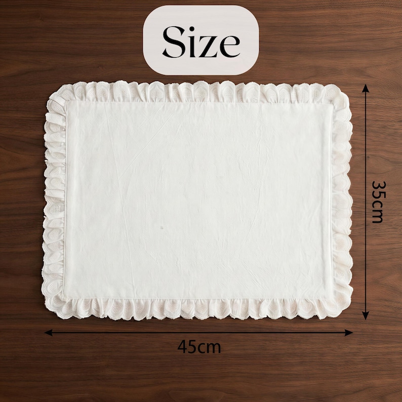 May include: A white rectangular placemat with a ruffled edge. The placemat is 17.7 inches long and 13.8 inches wide. The word "Size" is in a white rounded rectangle in the top center of the image. The placemat is on a dark brown wooden surface.