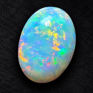 May include: An oval-shaped cabochon opal gemstone featuring a translucent white base with vibrant flashes of iridescent blue, green, yellow, and orange color play throughout the polished, smooth, and rounded surface of the stone.