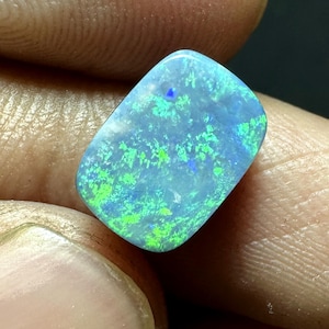May include: A rectangular loose gemstone with a polished surface, displaying a vibrant play of color with bright neon green and electric blue flashes set against a translucent, light blue base, showcasing a distinct iridescent pattern.