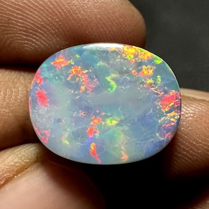 May include: Oval-shaped opal gemstone with a vibrant play of color. The stone displays flashes of red, orange, yellow, and green against a milky white and blue base. The opal is smooth and polished, showcasing its natural beauty.