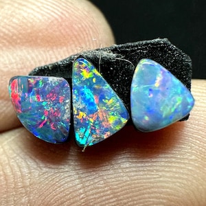 May include: Three triangular-shaped opals featuring vibrant flashes of blue, green, red, and yellow color play. The stones are polished with smooth, rounded edges and exhibit a high-luster finish, displaying intense iridescence across their surfaces.