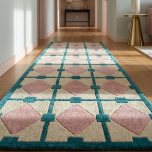 May include: A patterned hallway rug with a teal border, cream-colored squares, and pink diamond shapes. The rug is placed on a wooden floor in a hallway with light blue and pink walls. The rug's design is geometric.