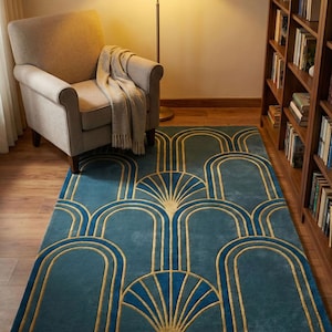 May include: A teal area rug with a gold art deco design. The rug features a repeating pattern of arches and fan-like shapes. The rug is placed in a room with a chair, lamp, and bookshelf.