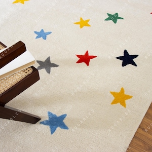 May include: Cream-colored rug with a pattern of colorful stars in blue, yellow, red, green, and gray. A dark brown wooden chair with a woven seat and a stack of books is in the corner of the image.