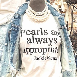 May include: White t-shirt with the text "Pearls are always appropriate - Jackie Kennedy" printed in black. The shirt is being worn by a mannequin with a pearl necklace.