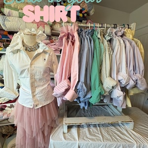 Puede incluir: Una taza de cerámica blanca con asa negra y el texto "But First, Coffee" en negrita negra. La taza se encuentra sobre un fondo borroso, sugiriendo un ambiente acogedor.