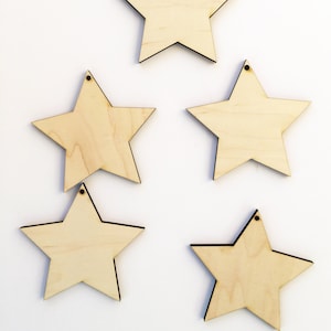 May include: Five unfinished wooden stars with a hole at the top. The stars are all the same size and shape, and they are arranged in a staggered pattern.