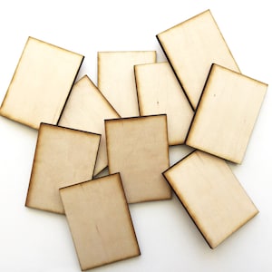 May include: A set of ten unfinished wooden rectangular tags with slightly burnt edges. The tags are arranged in a pile on a white background.