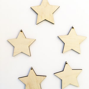 Pu&ograve; includere: Cinque stelle di legno non finite con un foro in cima. Le stelle sono tutte della stessa dimensione e forma, e sono disposte in uno schema sfalsato.