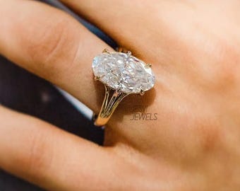 May include: A gold ring with a large, oval-cut diamond. The diamond is clear and sparkling, set on a delicate gold band. The ring is on a finger, with the brand name "JESVI JEWELS" visible.