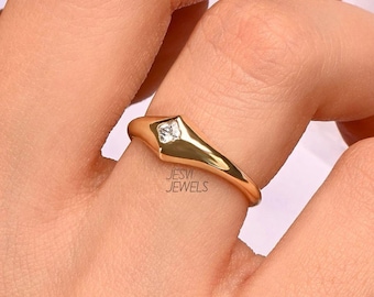 May include: A gold ring featuring a square, clear gemstone in a geometric setting. The ring is on a finger, with the brand name "JESVI JEWELS" visible.