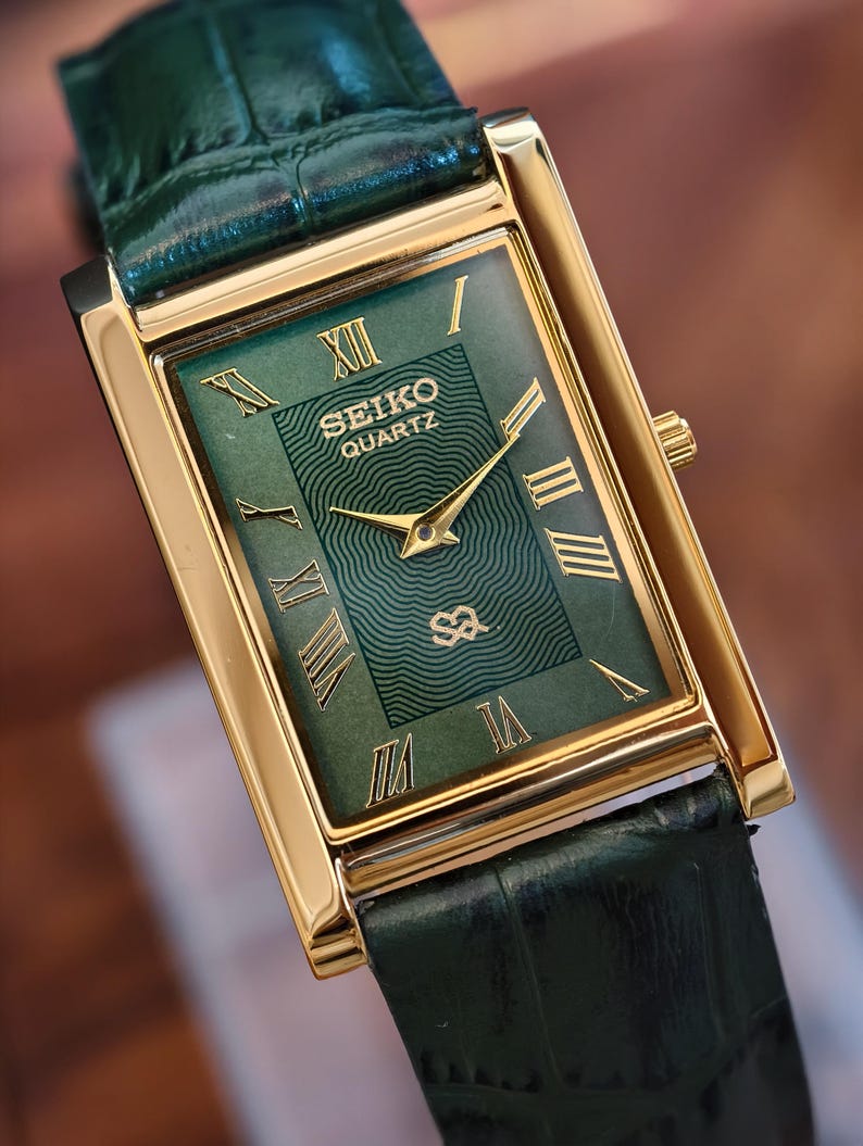 May include: A rectangular Seiko Quartz watch with a gold-tone case and a green dial. The dial features gold Roman numerals and hands. The watch has a green leather strap.