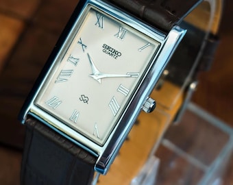 Reloj Seiko vintage de cuarzo rectangular elegante: esfera blanca, números romanos y correa de piel negra.