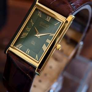 May include: A rectangular gold-toned Seiko Quartz watch with a green face and gold hands and Roman numerals. The watch has a brown leather strap with a crocodile pattern.