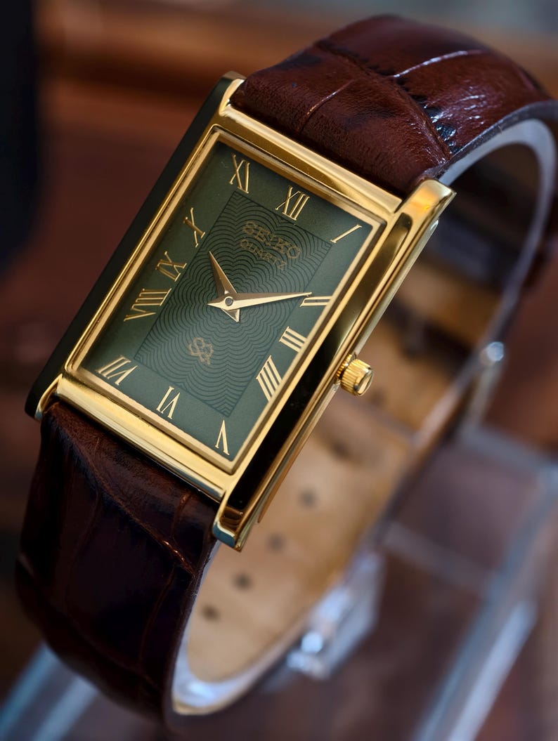 May include: A rectangular gold-toned Seiko Quartz watch with a green face and gold hands and Roman numerals. The watch has a brown leather strap with a crocodile pattern.