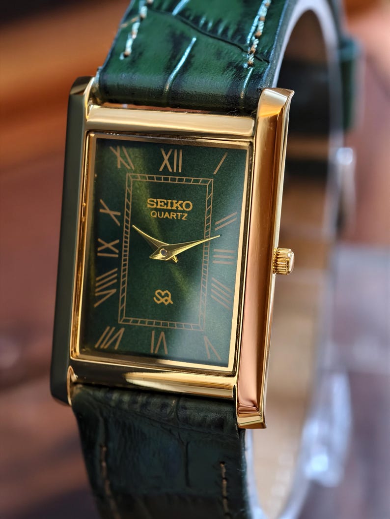 May include: A rectangular Seiko Quartz watch with a gold-tone case and a green dial. The watch features gold hands and Roman numeral hour markers. The watch has a green leather band.