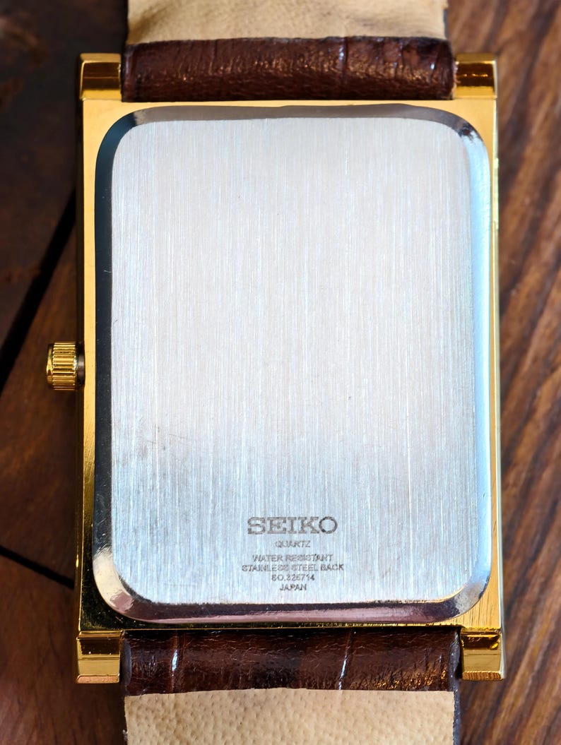 May include: A gold-coloured rectangular Seiko quartz watch with a brown leather strap. The watch back is stainless steel and features the Seiko logo and text indicating it is water-resistant. Made in Japan.
