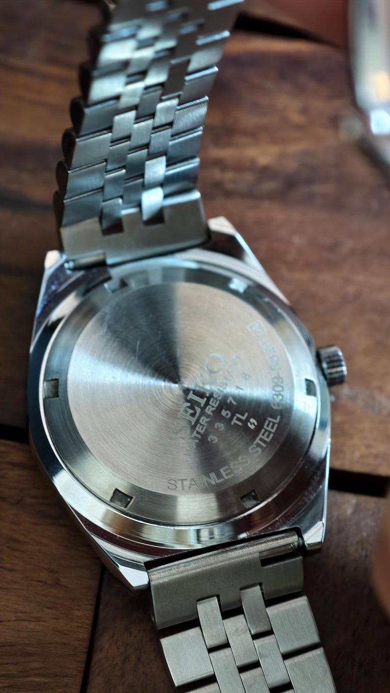 May include: Close-up of a stainless steel watch with a silver band. The watch face is visible, with the brand name "Seiko" and "Water Resistant" printed on it. The band has a woven design.