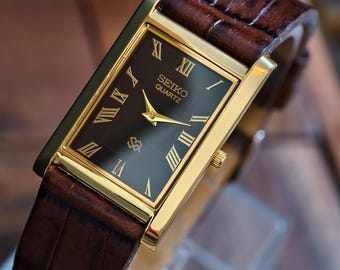 Reloj Seiko Tank vintage: delgado, tono dorado, esfera texturizada negra.