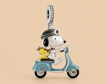 May include: A silver charm featuring a white dog wearing a black helmet and goggles, riding a blue scooter with a small yellow bird sitting on the back. The charm includes a bail at the top decorated with small clear stones for attachment.